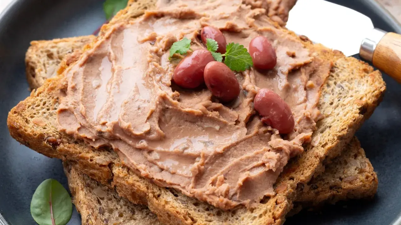 Pyszna pasta z czerwonej fasoli na chrupiących tostach, ozdobiona fasolkami i listkami ziół. Idealna na szybkie śniadanie.