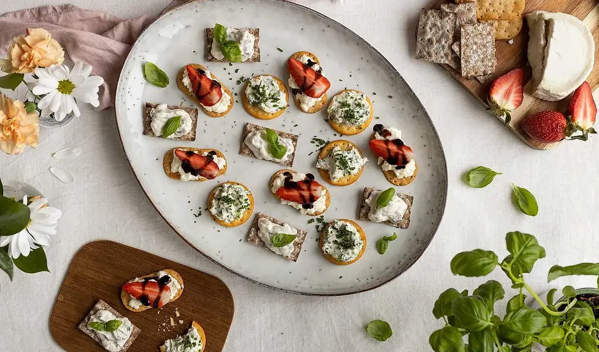 Vackra midsommar-snittar med ost, jordgubbar och örter på en stor tallrik. Perfekt för sommarfesten!