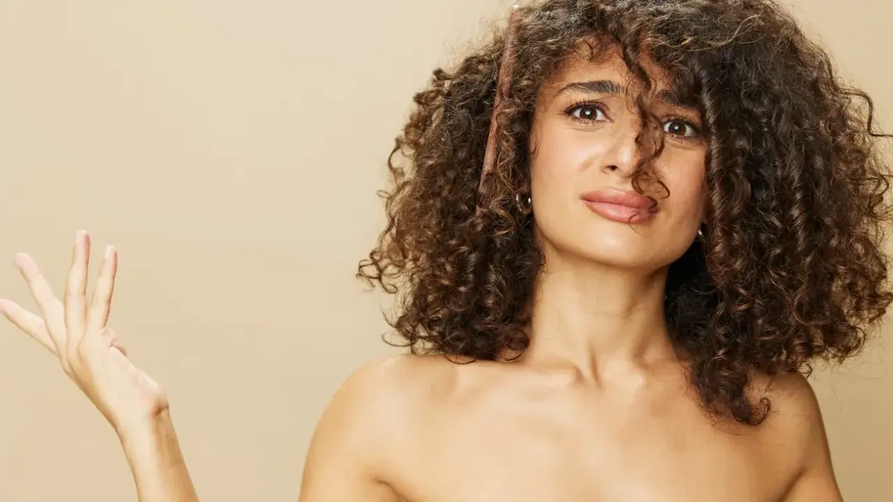Une femme aux cheveux bouclés tente de diminuer le volume de sa chevelure avec un peigne.