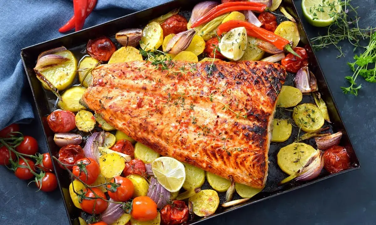 Pescado al horno con patatas, cebolla y tomate, asado a la perfección con hierbas frescas y un toque de limón.