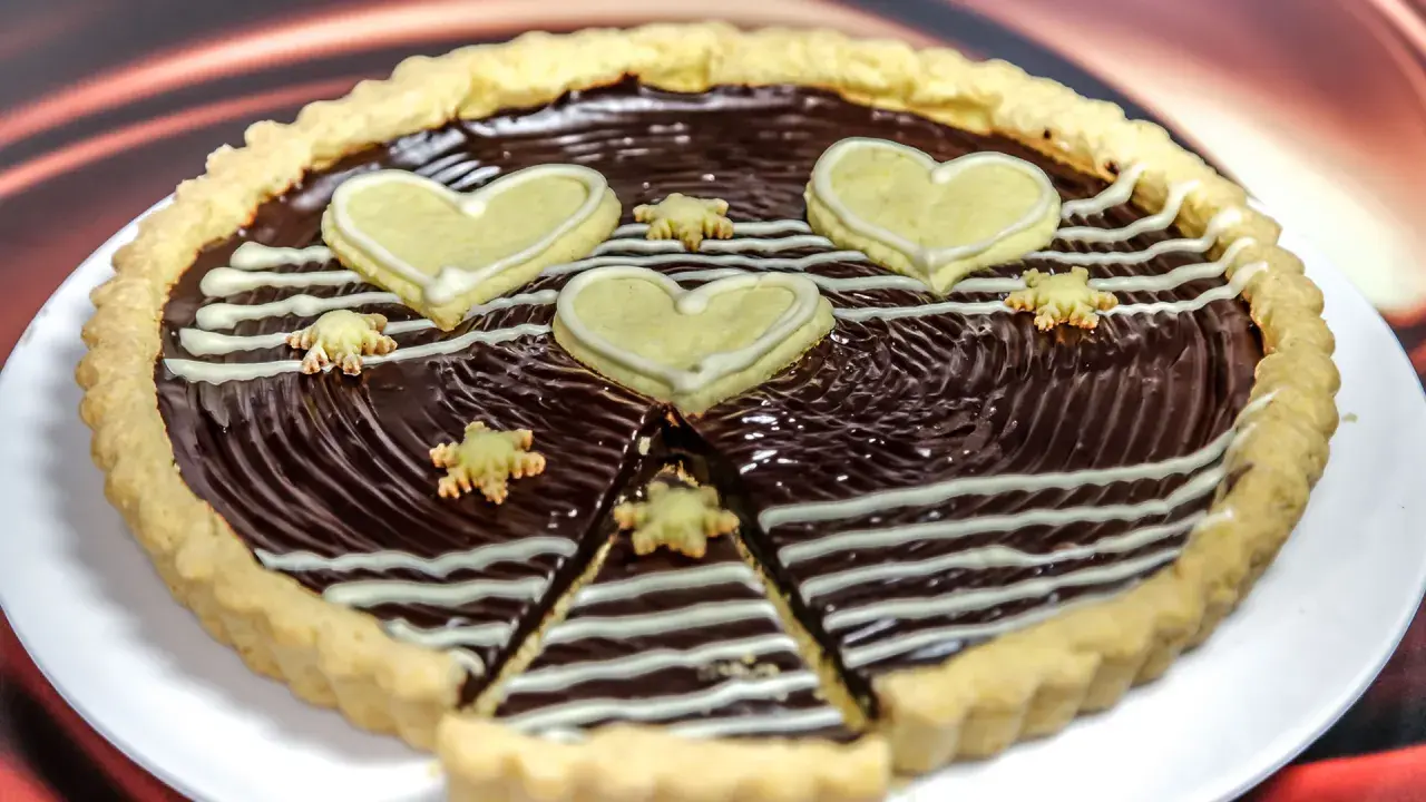 Una deliziosa crostata al cioccolato, decorata con cuori e fiorellini di pasta frolla, pronta per essere gustata.