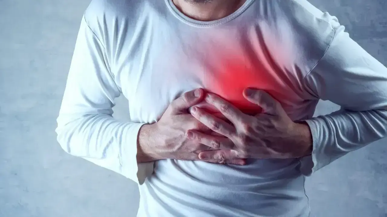 Mężczyzna trzyma się za klatkę piersiową, gdzie widoczny jest czerwony obszar bólu.