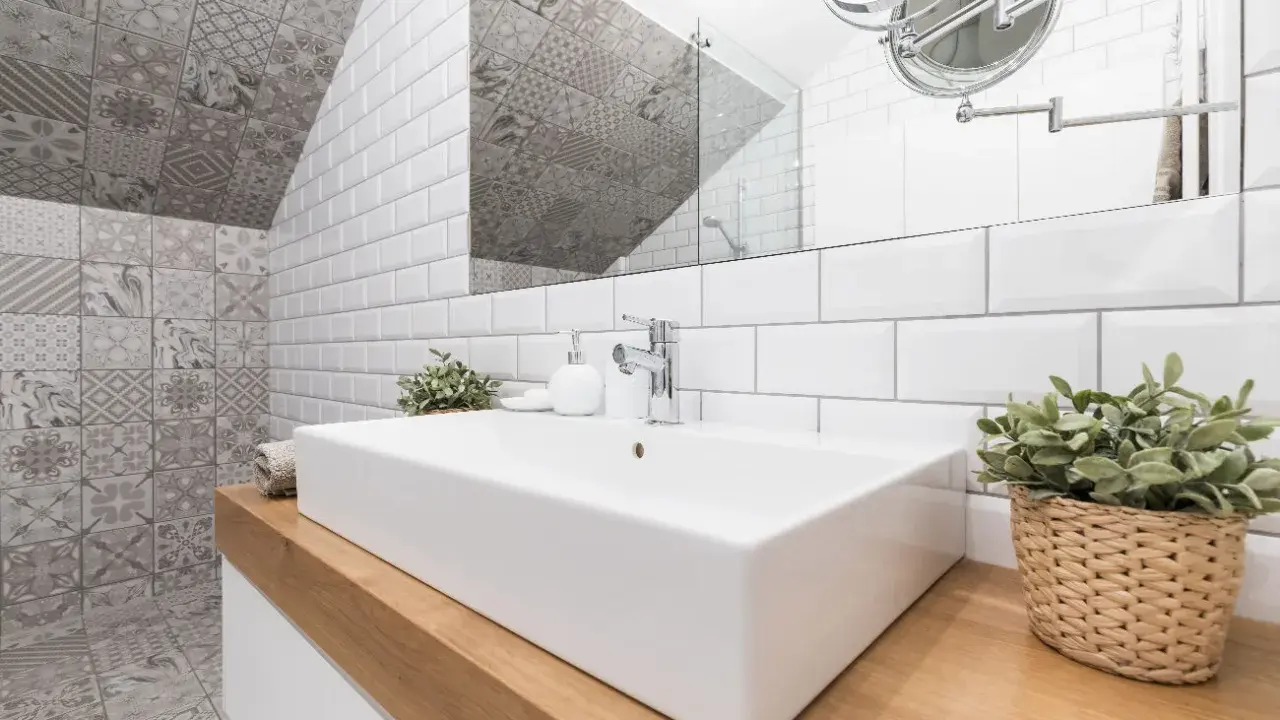 Salle de bain moderne avec lavabo rectangulaire, robinetterie chromée et un mur orné de **pose carrelage mural** patchwork gris et blanc.