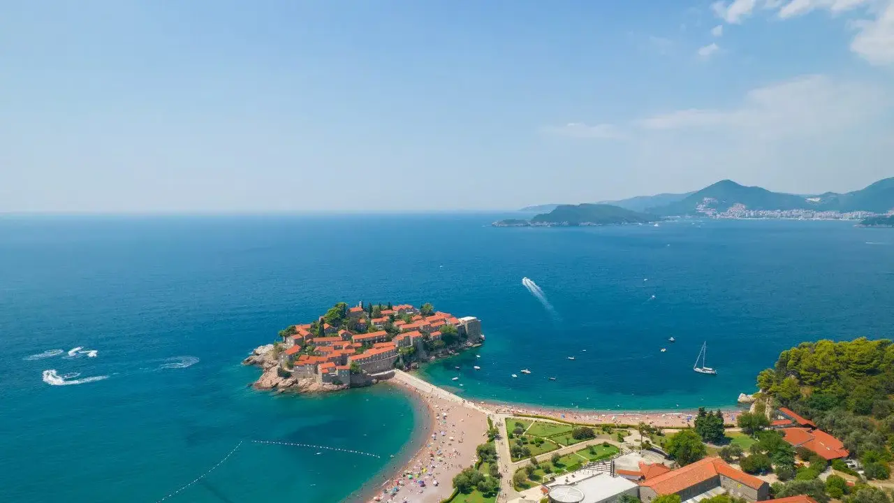 Malownicza wyspa z czerwonymi dachami połączona z lądem, otoczona turkusowym morzem i piaszczystymi plażami. Czarnogóra plaże zachwycają.