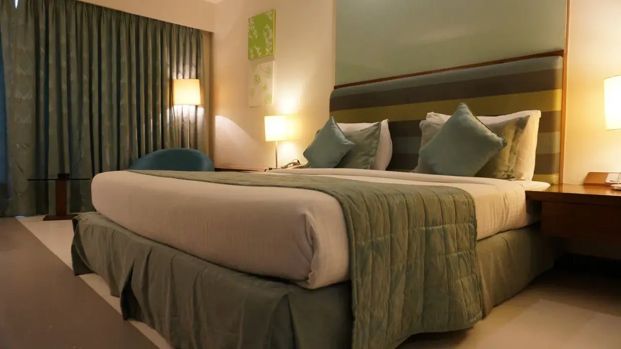 Ideas de iluminación para dormitorio de matrimonio: cama acogedora con lámparas de noche y cortinas verdes.
