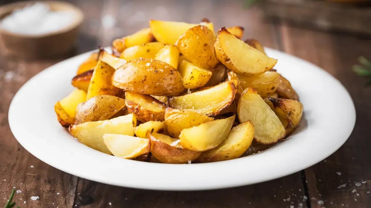 Patate al forno con buccia, dorate e croccanti, servite su un piatto bianco. Un contorno semplice e gustoso.