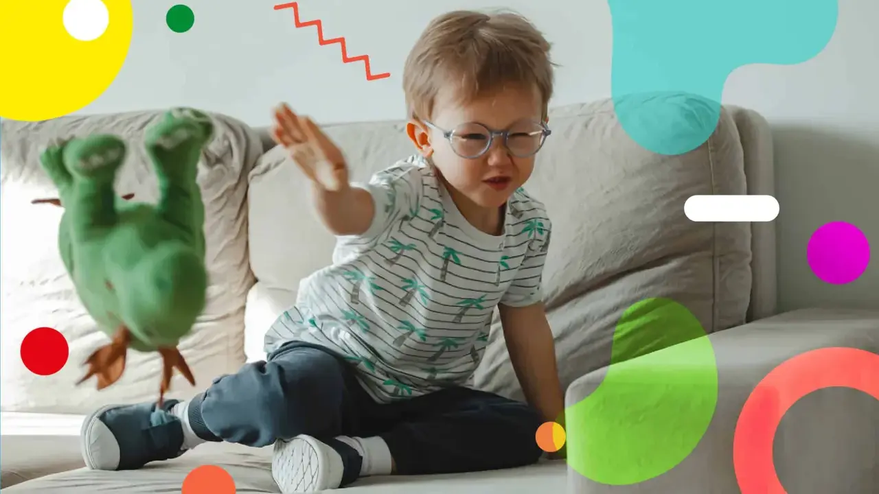 Un bambino super attivo gioca sul divano con un pupazzo verde. Le sue mani sono in movimento, pronto a interagire con il giocattolo.