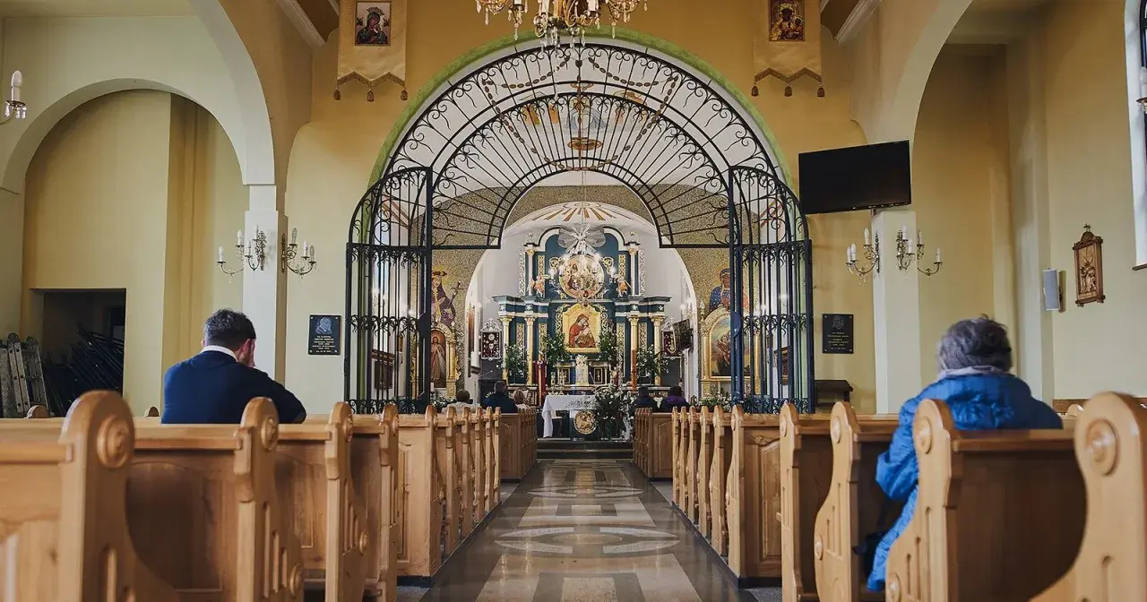 Wnętrze sanktuarium Matki Bożej Pięknej Miłości w Polańczyku. Wierni siedzą w ławkach, patrząc na ołtarz.