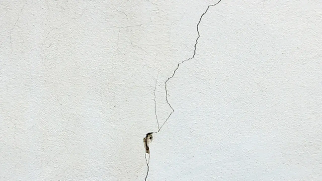 Una grieta fina y profunda recorre una pared blanca, mostrando diferentes tipos de grietas en techos y paredes.