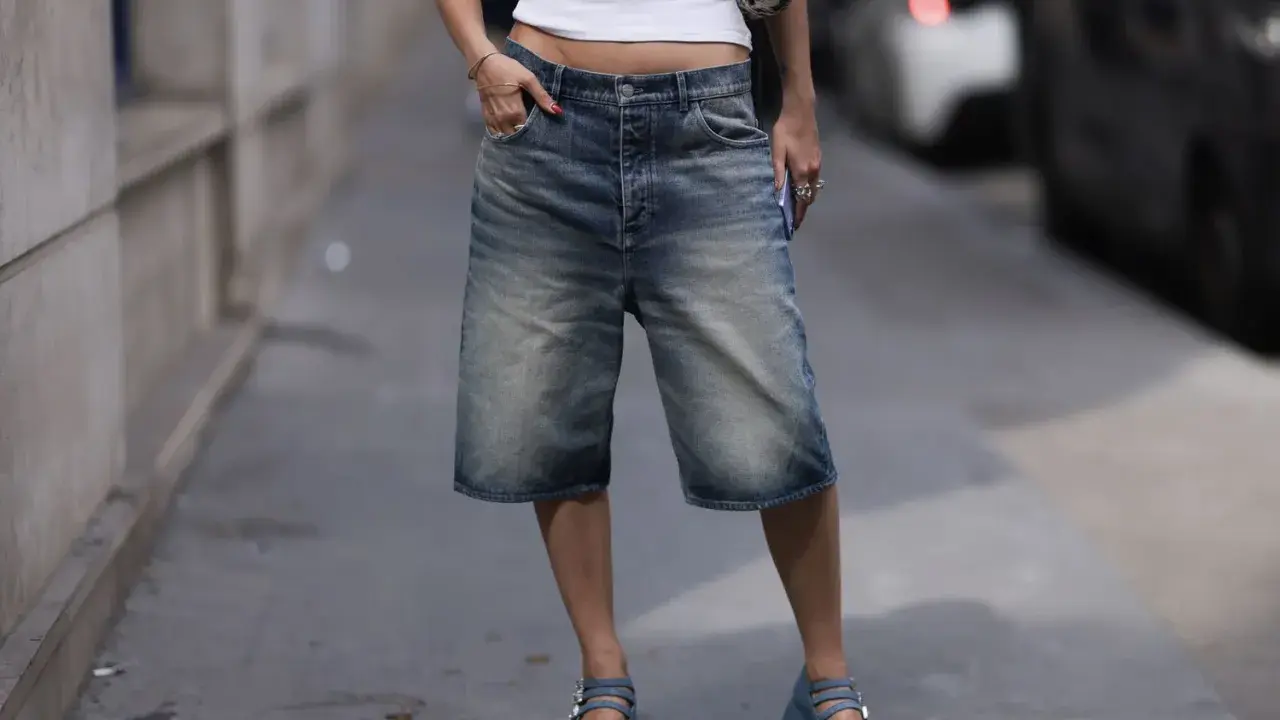 A person in denim bermuda shorts and a white crop top sports chunky blue platform Mary Janes, a nod to early 2000s shoe trends.