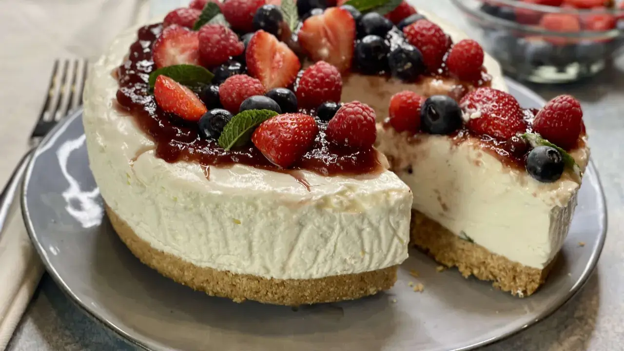 Deliziosa torta fredda allo yogurt, guarnita con fragole, lamponi, mirtilli e una colata di marmellata. Perfetta per un dessert estivo.