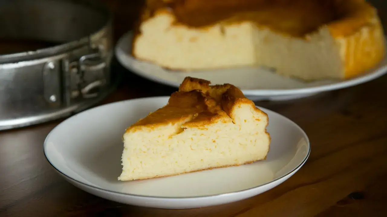 Puszysty sernik z mlekiem skondensowanym, z rumianą skórką, na talerzyku. Obok forma do pieczenia.