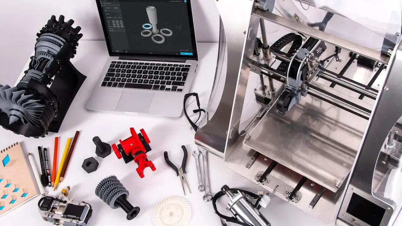 Il disegnatore CAD lavora su un laptop con un modello 3D, circondato da componenti stampati in 3D e strumenti.