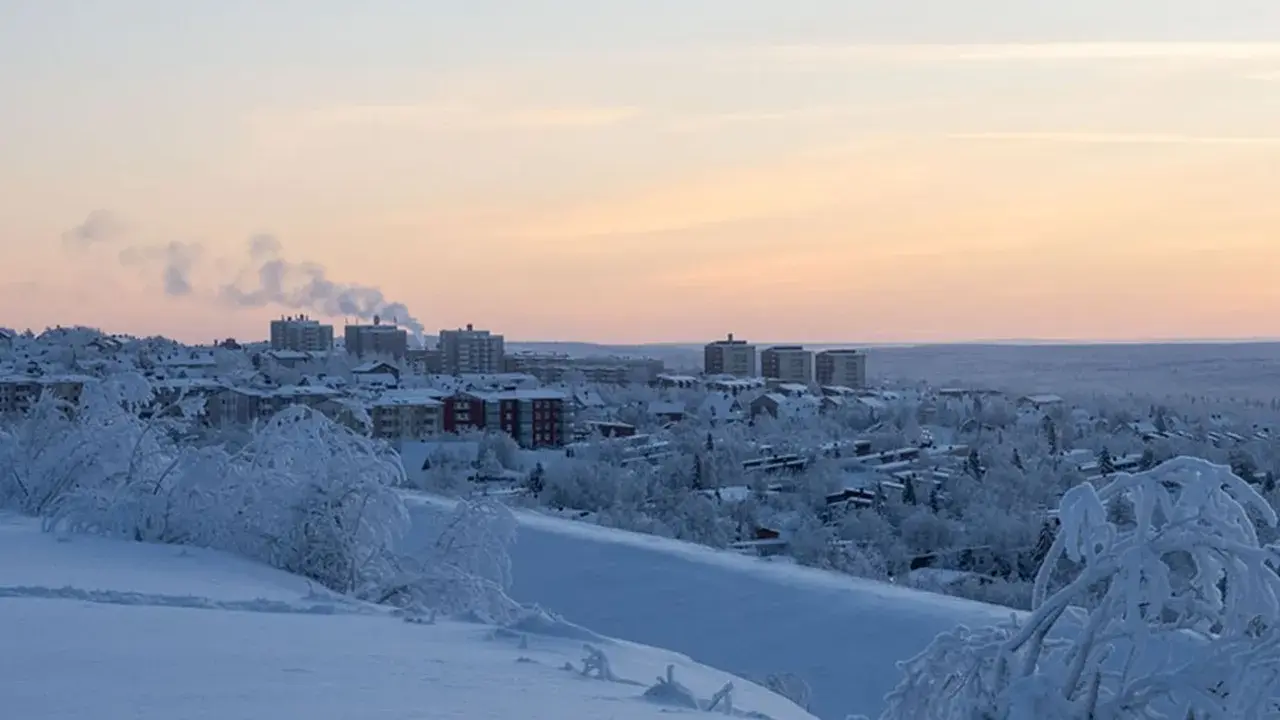 Vinterlandskap i lapponia svedese med snötäckta träd och byggnader i fjärran under en rosa solnedgång.