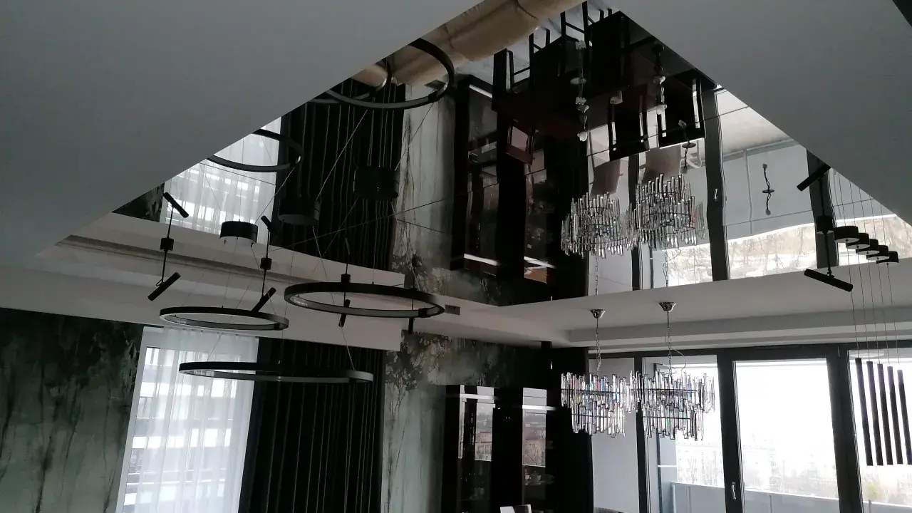Eleganckie lustro na suficie w sypialni odbija nowoczesne lampy i meble, tworząc wrażenie przestronności.