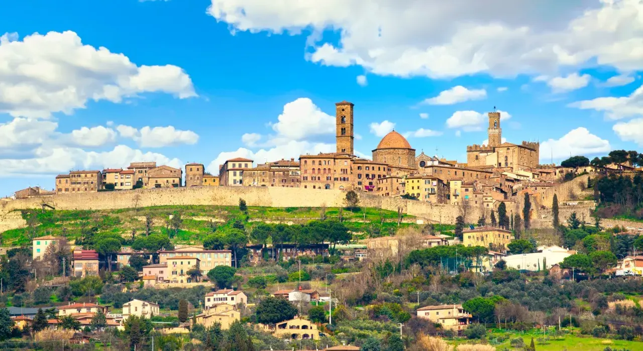 Panoramica di Volterra, dove si trova questo antico borgo toscano, con le sue torri e case arroccate sulla collina sotto un cielo azzurro con nuvole bianche.