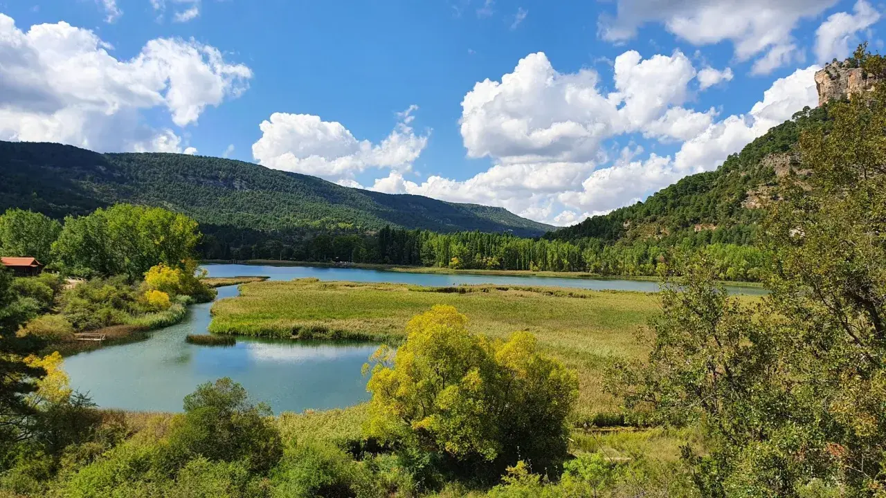 Paisaje de lagunas y montañas verdes, ideal para rutas senderismo Cuenca. Cielo azul con nubes blancas.