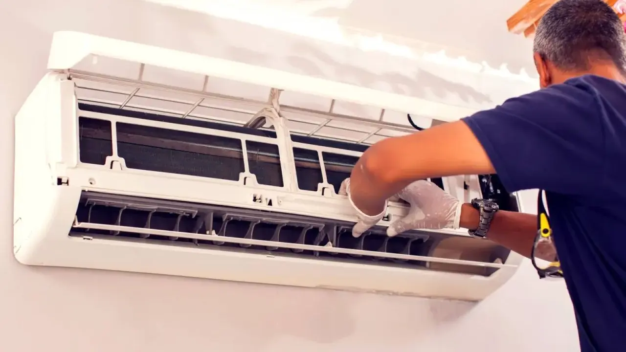Un technicien en gants blancs effectue le nettoyage de climatisation, ouvrant l'unité pour accéder aux composants internes.