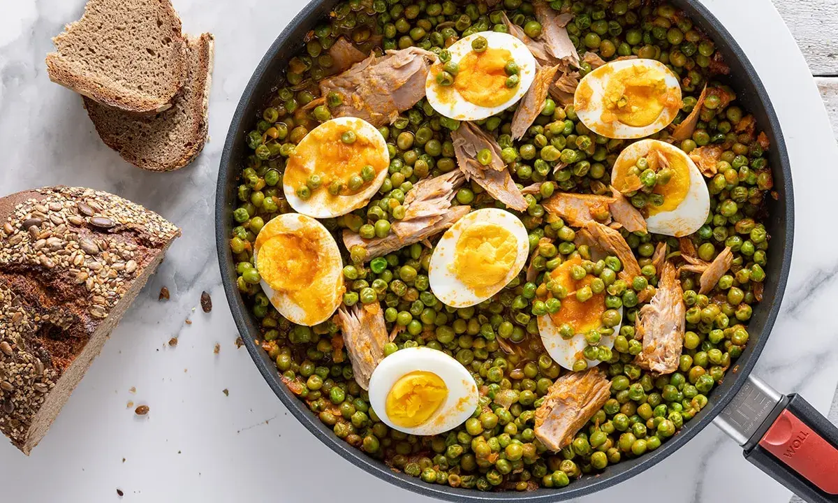 A skillet of peas and tuna with sliced hard-boiled eggs, served with bread.