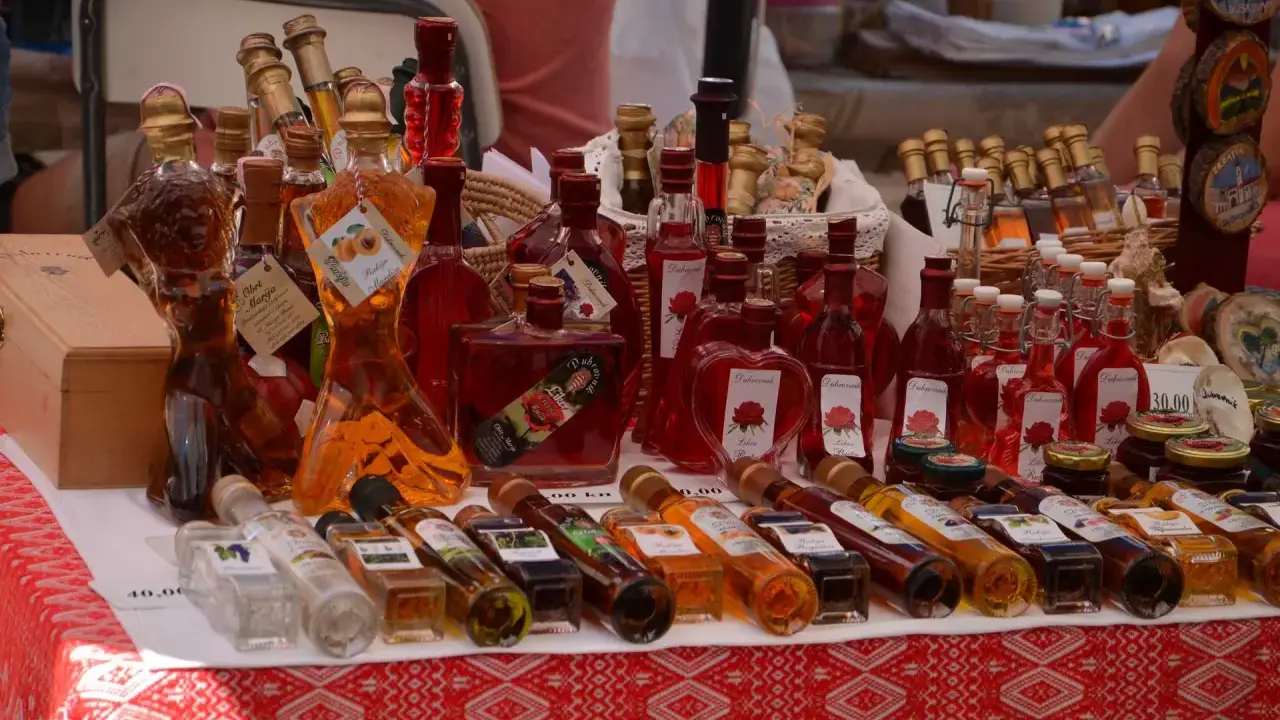 Różnorodne butelki z rakiją, w tym te w kształcie kobiecym, oferowane na targu. Co to rakija? To tradycyjny alkohol, często owocowy.