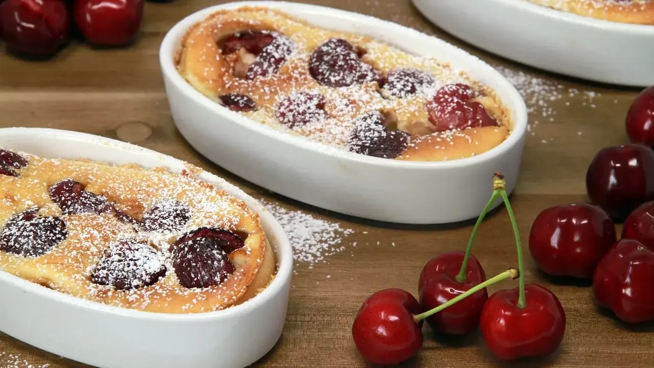 Deux clafoutis aux cerises, une spécialité auvergnate sucrée, saupoudrés de sucre glace, avec des cerises fraîches sur le côté.