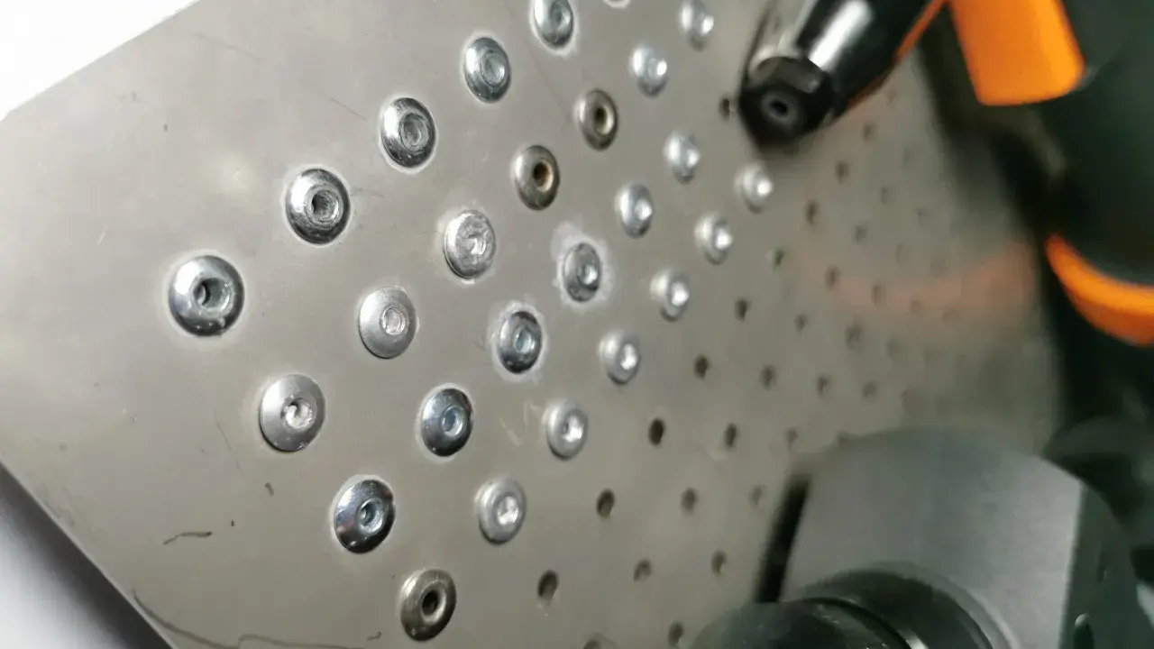 Metalowa płyta z rzędami nitów, narzędzie do nitowania ręcznego w akcji.
