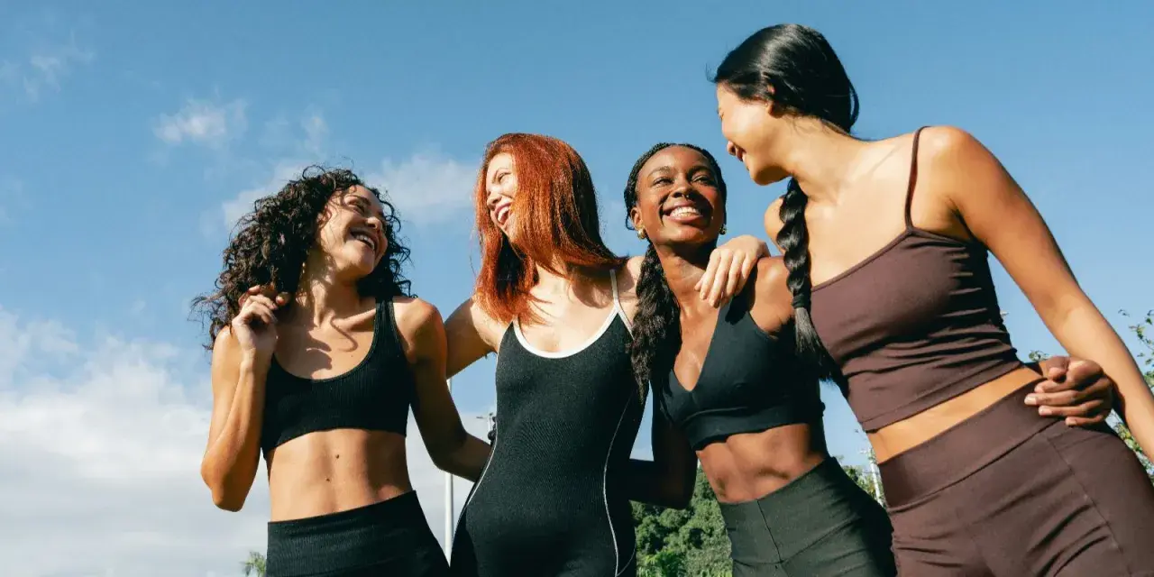 Quatre femmes souriantes, en tenue de sport, profitent du soleil. Leurs abdos sont visibles, suggérant une pratique comme l'abdo hypopressif.