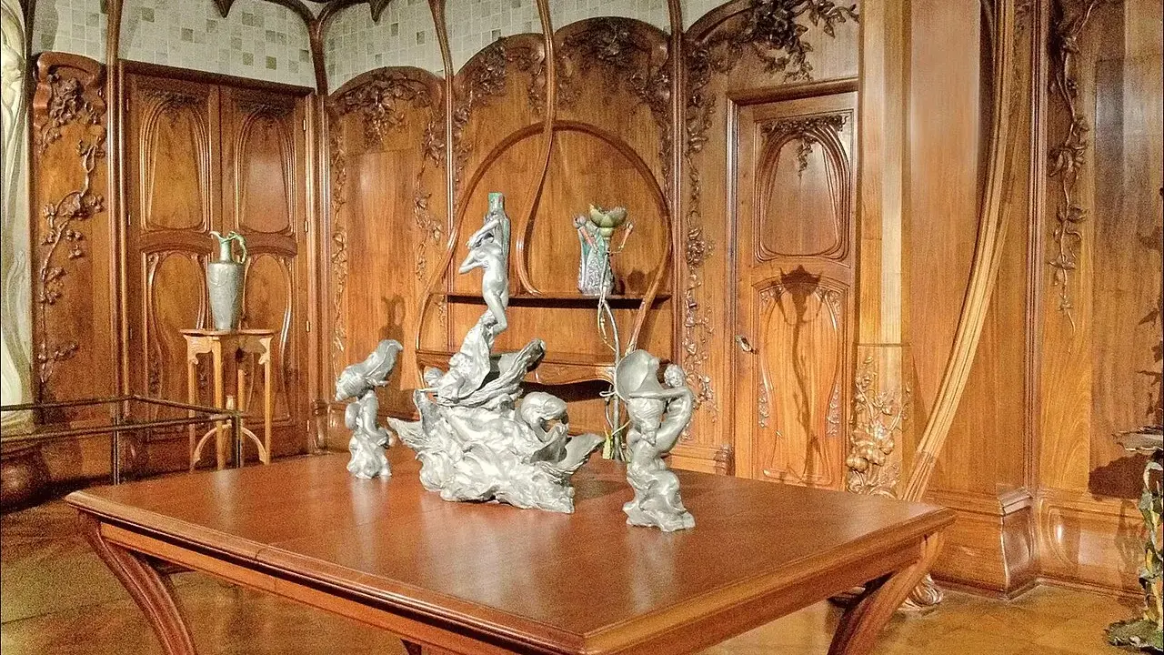 Intérieur Art Nouveau orné de boiseries sculptées, avec une table en bois et des sculptures, évoquant l'œuvre d'Alexandre Charpentier.