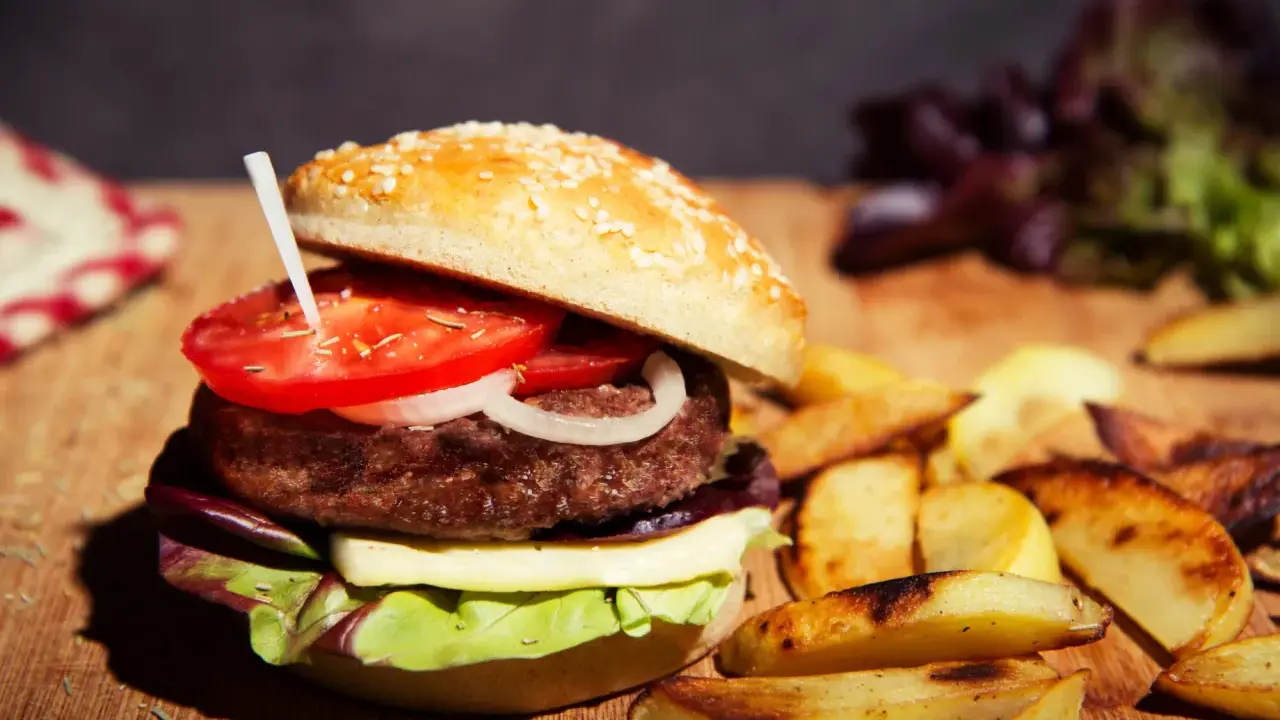 Burger maison avec pain aux graines, tomate, oignon, fromage et salade. Accompagné de frites. Une recette pain burger sans gluten à essayer !