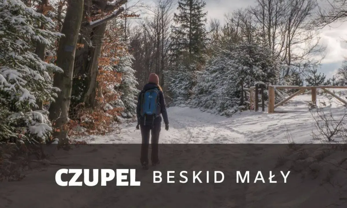 Kobieta w zimowej czapce i plecaku idzie zasypaną śniegiem trasą na Czupeł w Beskidzie Małym.