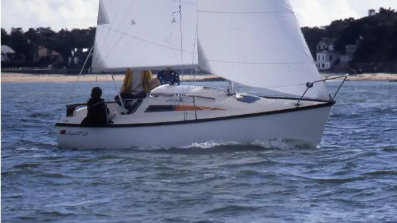 Voilier blanc naviguant sur une mer agitée, avec deux personnes à bord. Les premiers 18 avis sur ce modèle de bateau sont positifs.