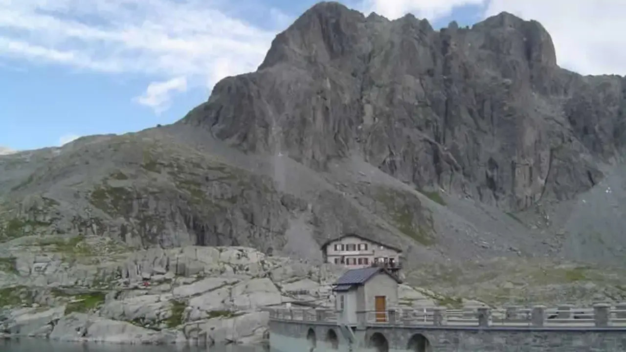 Rifugio sul lago della Vacca, con imponente parete rocciosa alle spalle.