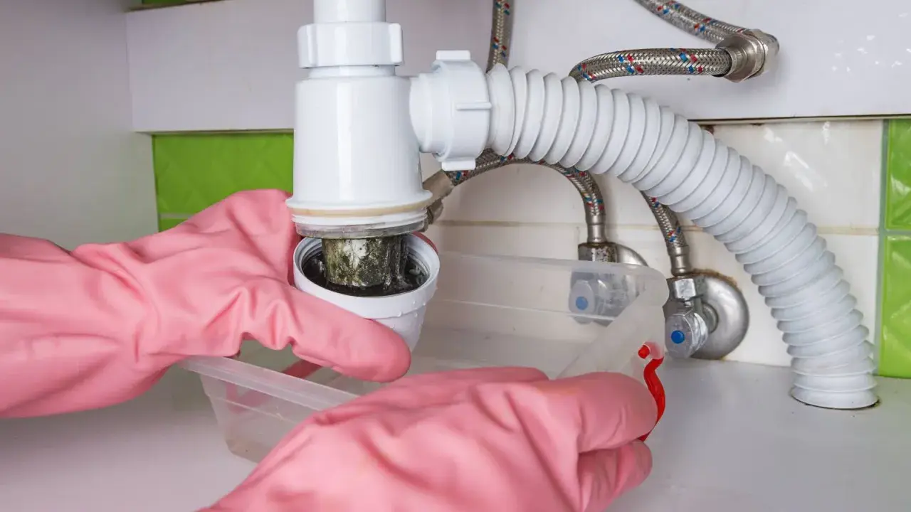 Mains de nettoyage rose démontant le siphon de lavabo bouché. Schéma montage siphon lavabo.