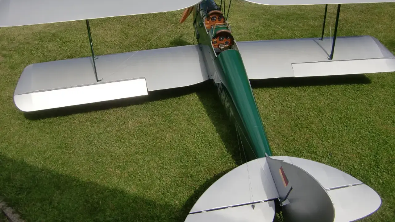 Ein detailgetreues Tiger Moth RC-Modellflugzeug mit silbernen Flügeln und grünem Rumpf steht auf einer grünen Wiese.