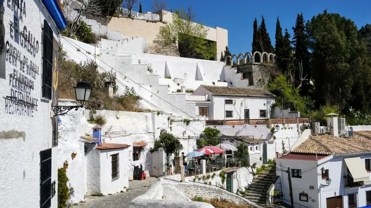 Weiße Häuser und Terrassen im Sacromonte, Granada, mit Kopfsteinpflaster und blühenden Pflanzen.