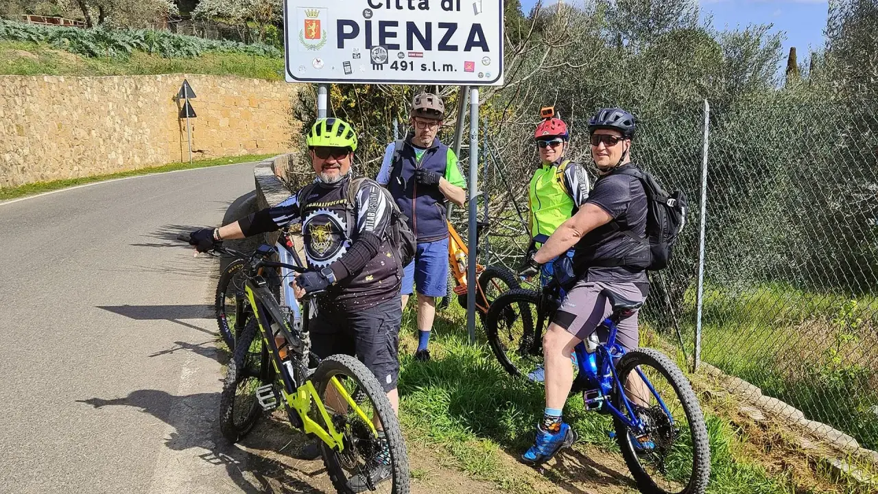 Quattro ciclisti si fermano per una foto con il cartello "Città di Pienza" durante un'avventura in bici nel Val d'Orcia.