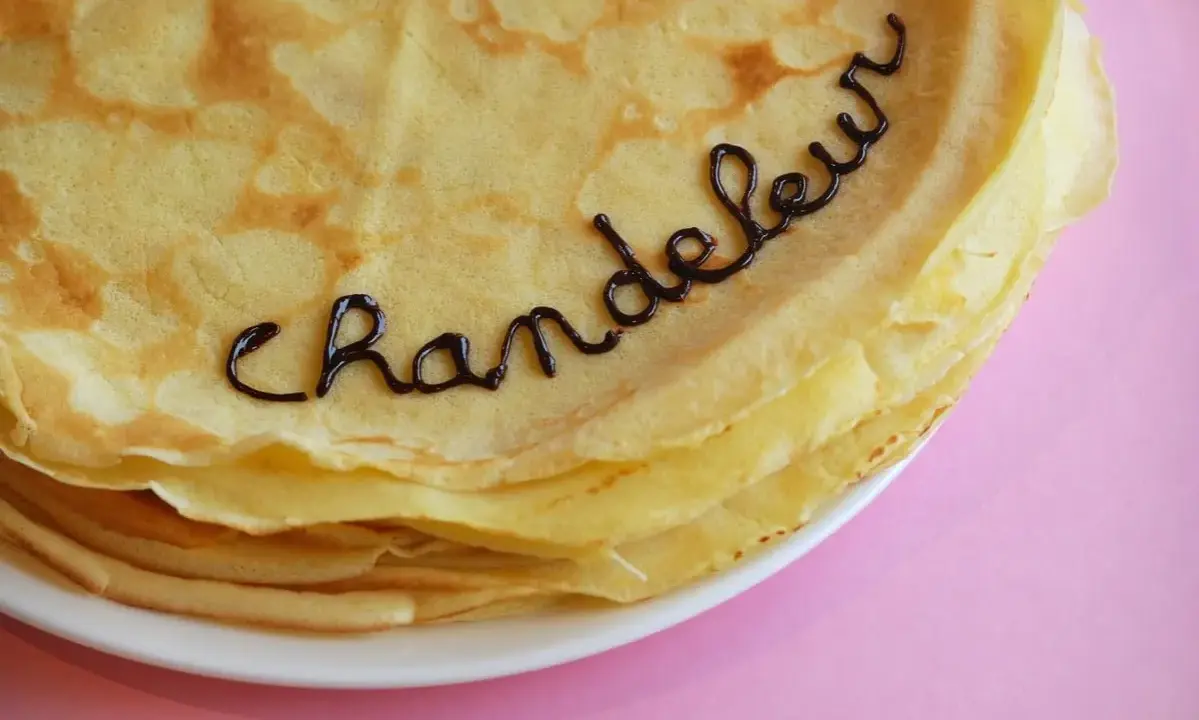 Une pile de crêpes dorées, décorées avec du chocolat formant le mot "Chandeleur". Un délice pour célébrer qu'est-ce que la Chandeleur.