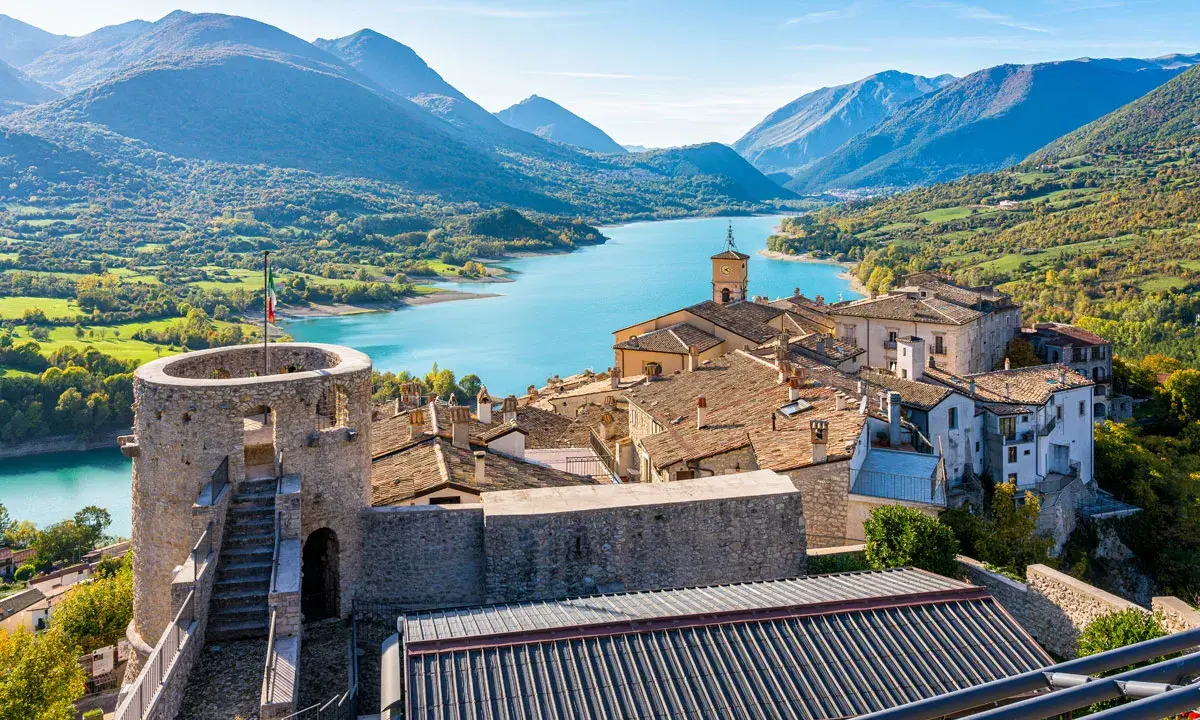 Borgo medievale con torre e lago turchese, incastonato tra i monti dell'Abruzzo.