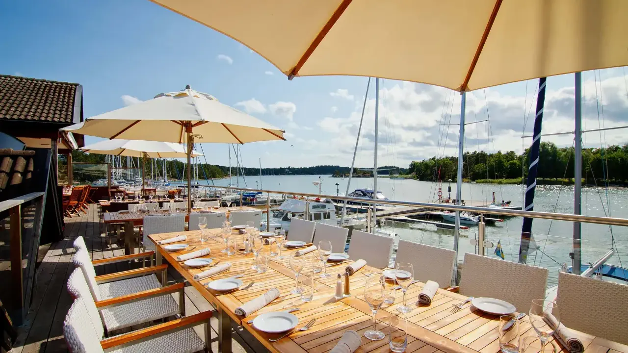 Väl dukade bord på en restaurang vid havet med segelbåtar i bakgrunden.