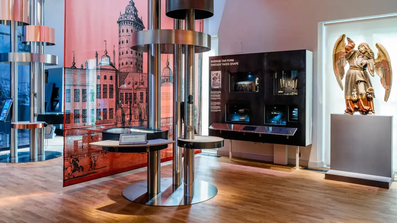 Utställning på ekonomiska museet med en stor illustration av en stad, en skulptur av en ängel och interaktiva displayer.