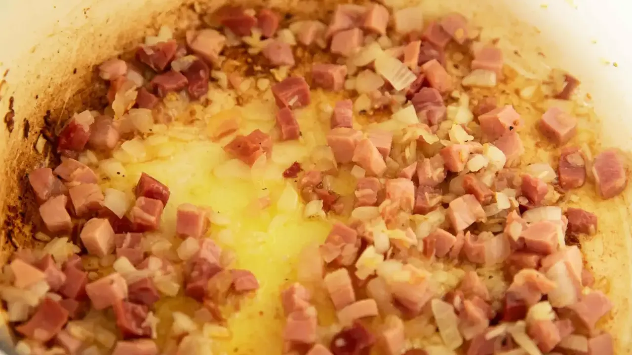 Guisantes con jamón y cebolla dorándose en una sartén con aceite. Un plato tradicional español.