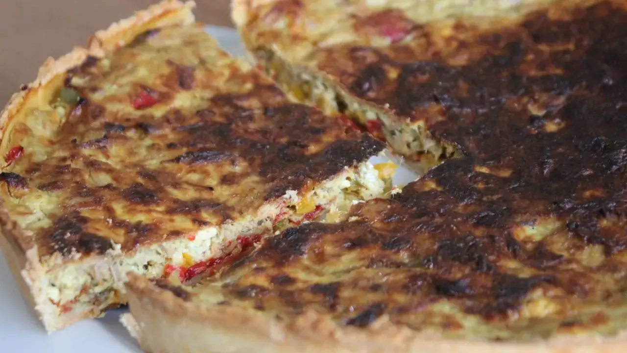 Une part de quiche poivron feta dorée, avec des morceaux de poivrons colorés et de feta crémeuse dans sa garniture.