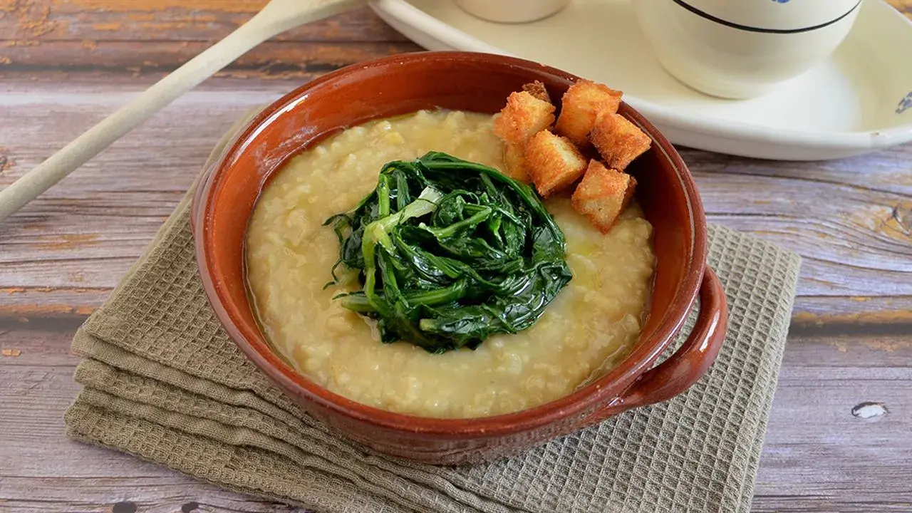 Piatto di fave e cicoria, una crema gialla con verdura verde al centro e crostini dorati.