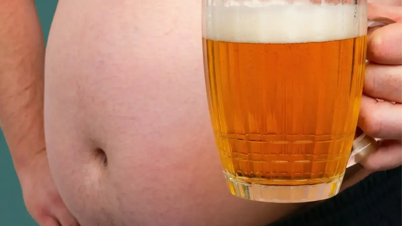Ein Bierbauch, der zeigt, dass Bier dick macht. Eine Hand hält ein Glas Bier vor dem Bauch.