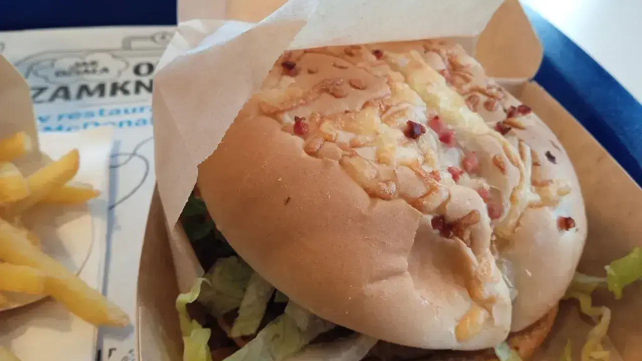 Pyszny burger drwala z chrupiącym bekonem i serem, w papierowym opakowaniu, obok porcji frytek.