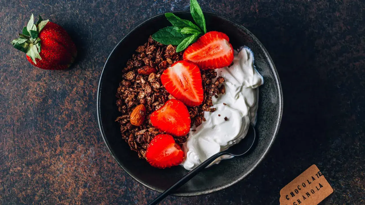 Schüssel mit Schokoladengranola, frischen Erdbeeren und cremigem Skyr oder Magerquark, garniert mit Minze.