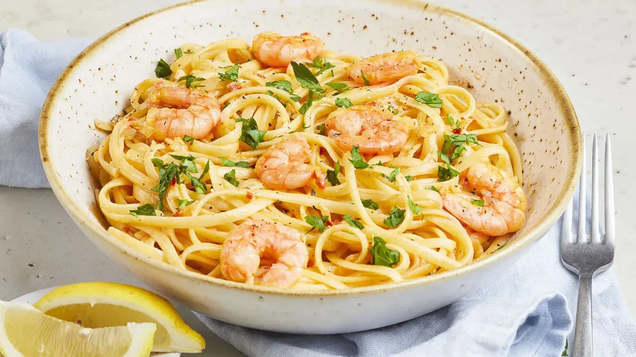 Eine Schüssel mit Spaghetti mit Garnelen, garniert mit Petersilie und Chiliflocken. Dazu Zitronenspalten und eine Gabel.