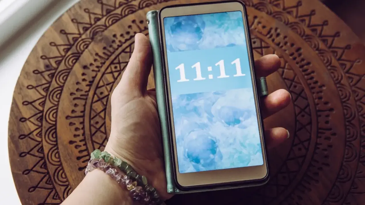 Dłoń trzyma telefon z wyświetloną godziną 11:11, co dla wielu ma szczególne znaczenie.