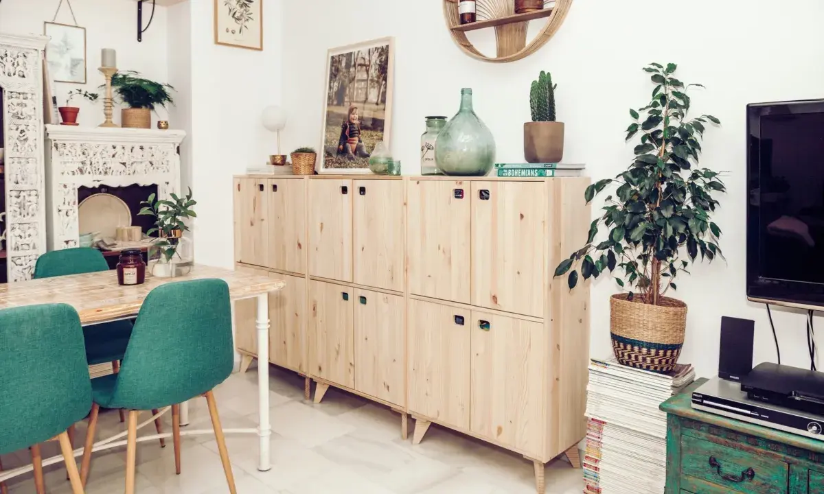 Muebles de madera clara con tiradores verdes, una mesa con sillas turquesas y una chimenea decorada. Inspiración para tu gama de colores para pintar muebles de madera.