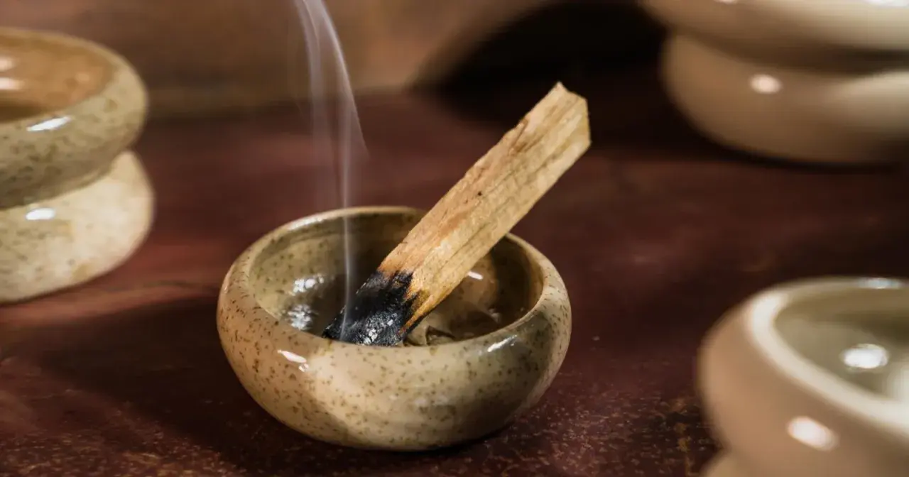 Dymiący patyczek palo santo w ceramicznej miseczce. Zastanawiasz się, palo santo co to? To święte drzewo używane do oczyszczania przestrzeni.
